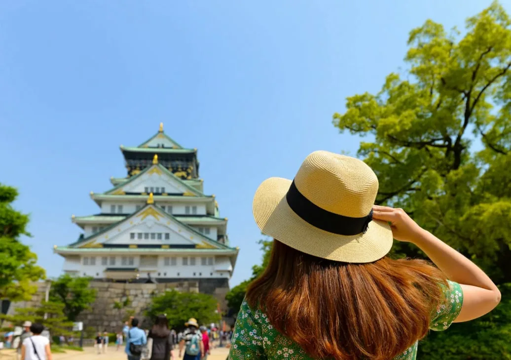 大阪城の天守閣を見上げる麦わら帽子の旅行者